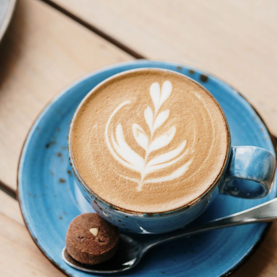 Latte with rosetta art in a blue ceramic cup, with a biscuit on the saucer