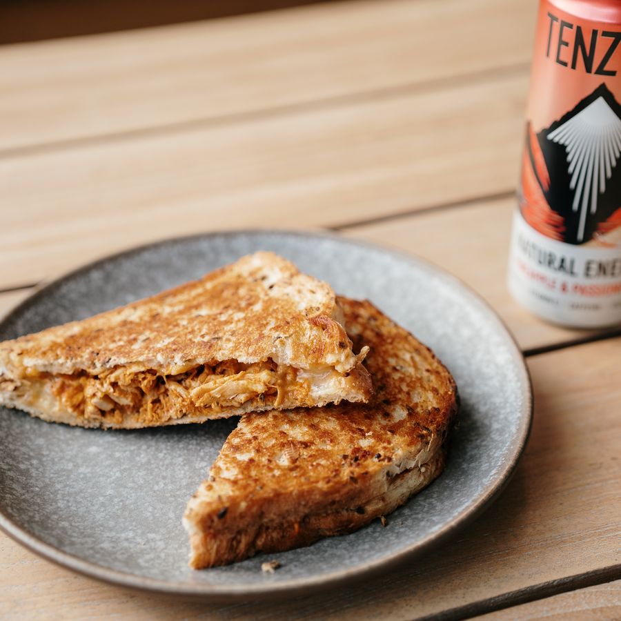 Toasted chicken sandwich cut in half on a stoneware plate, served with a cold drink