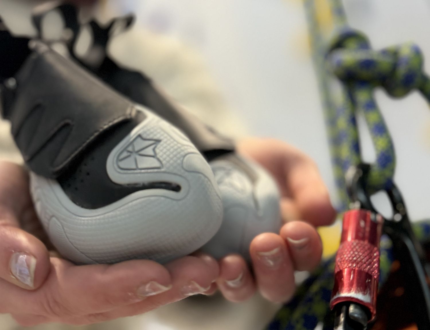 Hands holding out a climbing shoe at Beta Park at the Hub, with a rope and a red locking carabiner hanging alongside